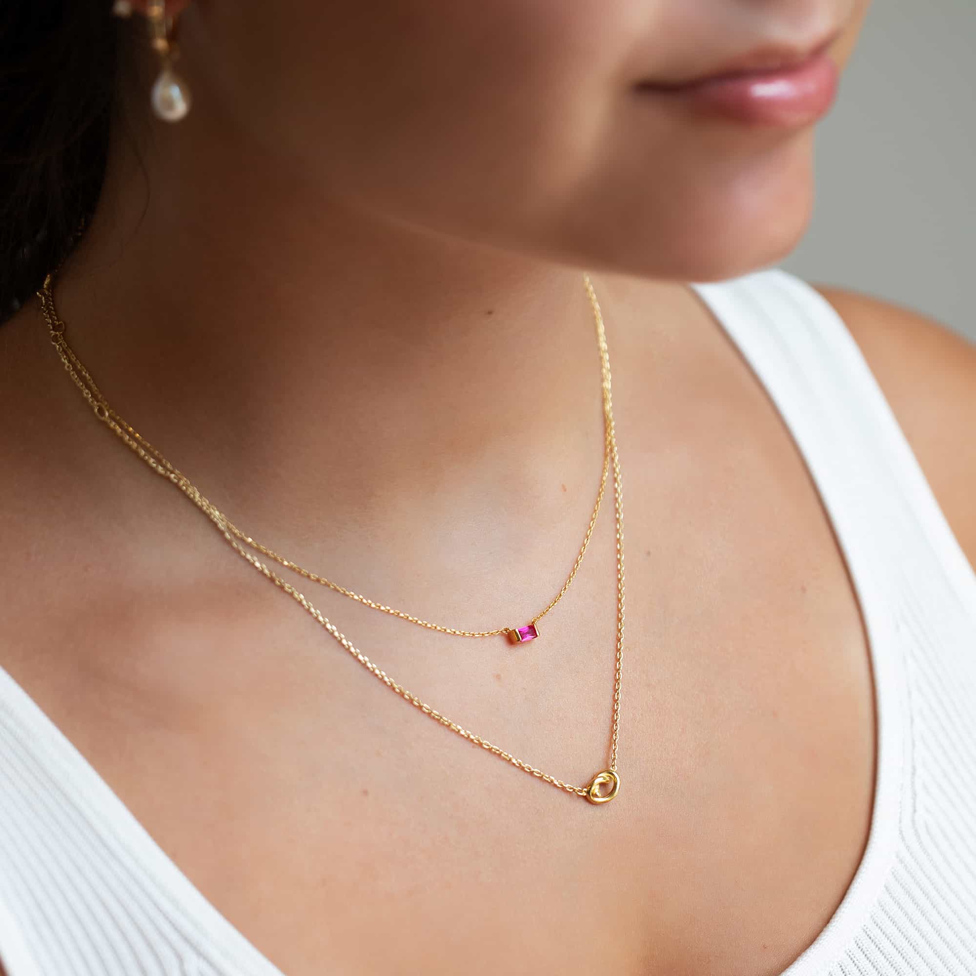 Gold vermeil baguette ruby necklace with a small red stone, shown on a model's neckline