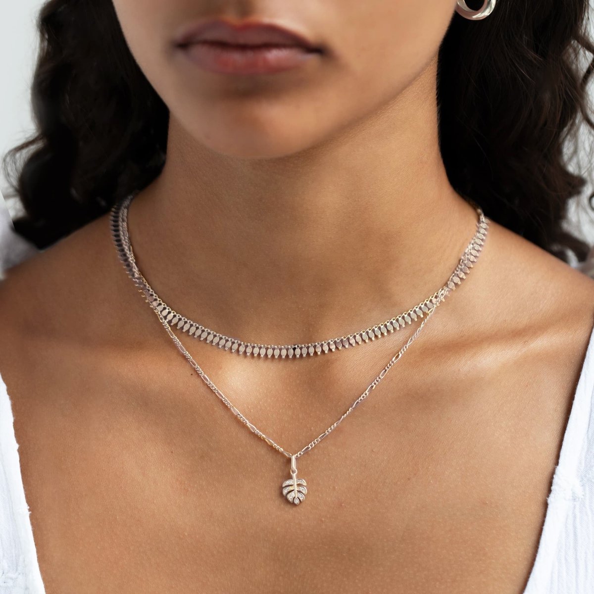 Sterling silver monstera leaf pendant on a chain, shown layered on a model's neckline