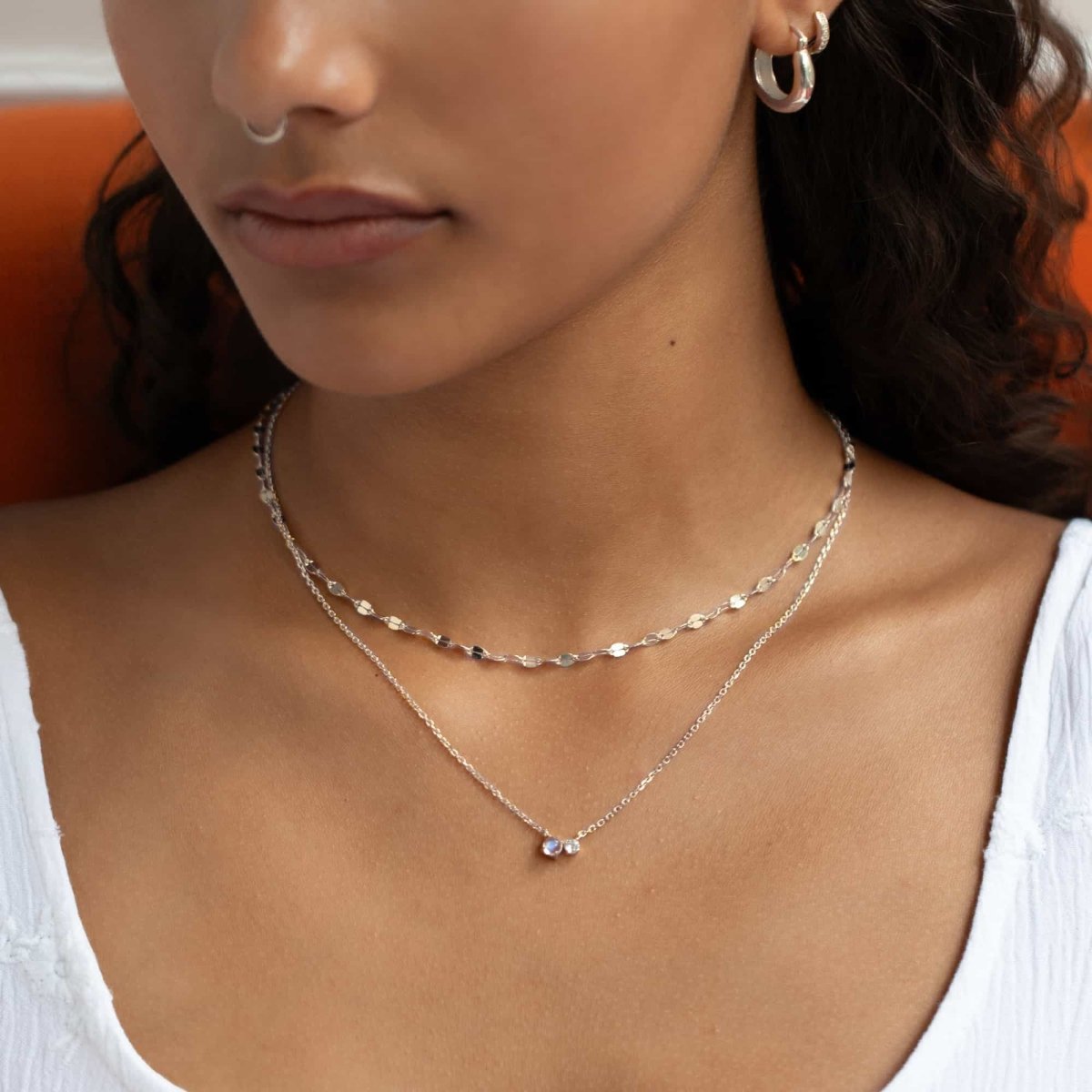 Sterling silver duet necklace with a moonstone and a clear stone, shown layered on a model's neckline