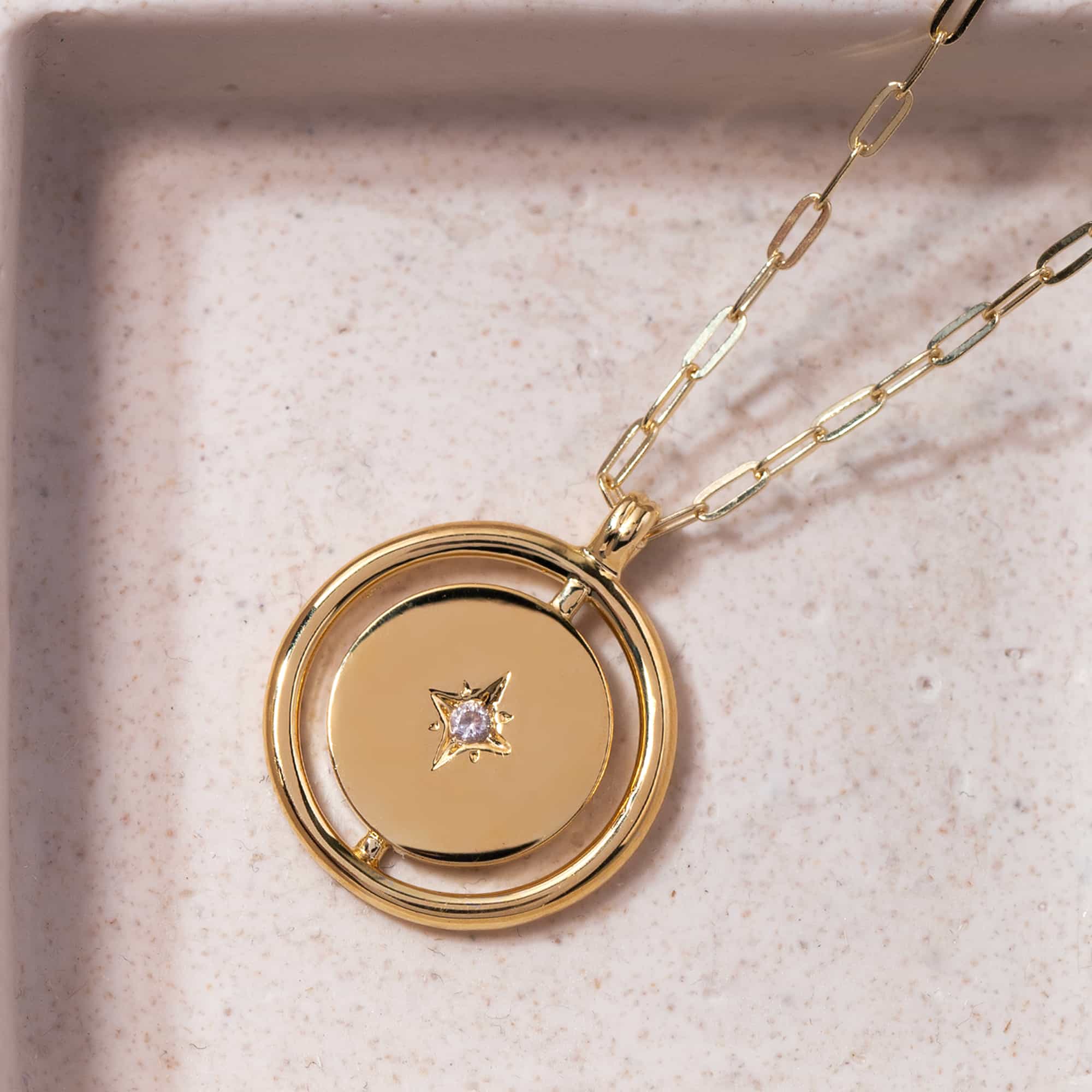 Gold vermeil Northern Star disc pendant with a star-set clear stone, close-up detail on a cream background