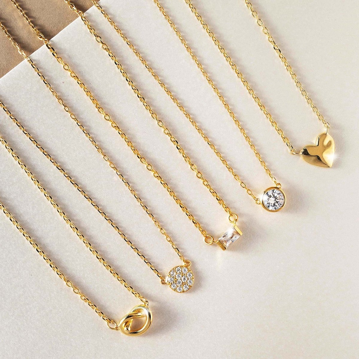Gold vermeil love knot necklace shown with other pendant necklaces, including a clear stone and heart
