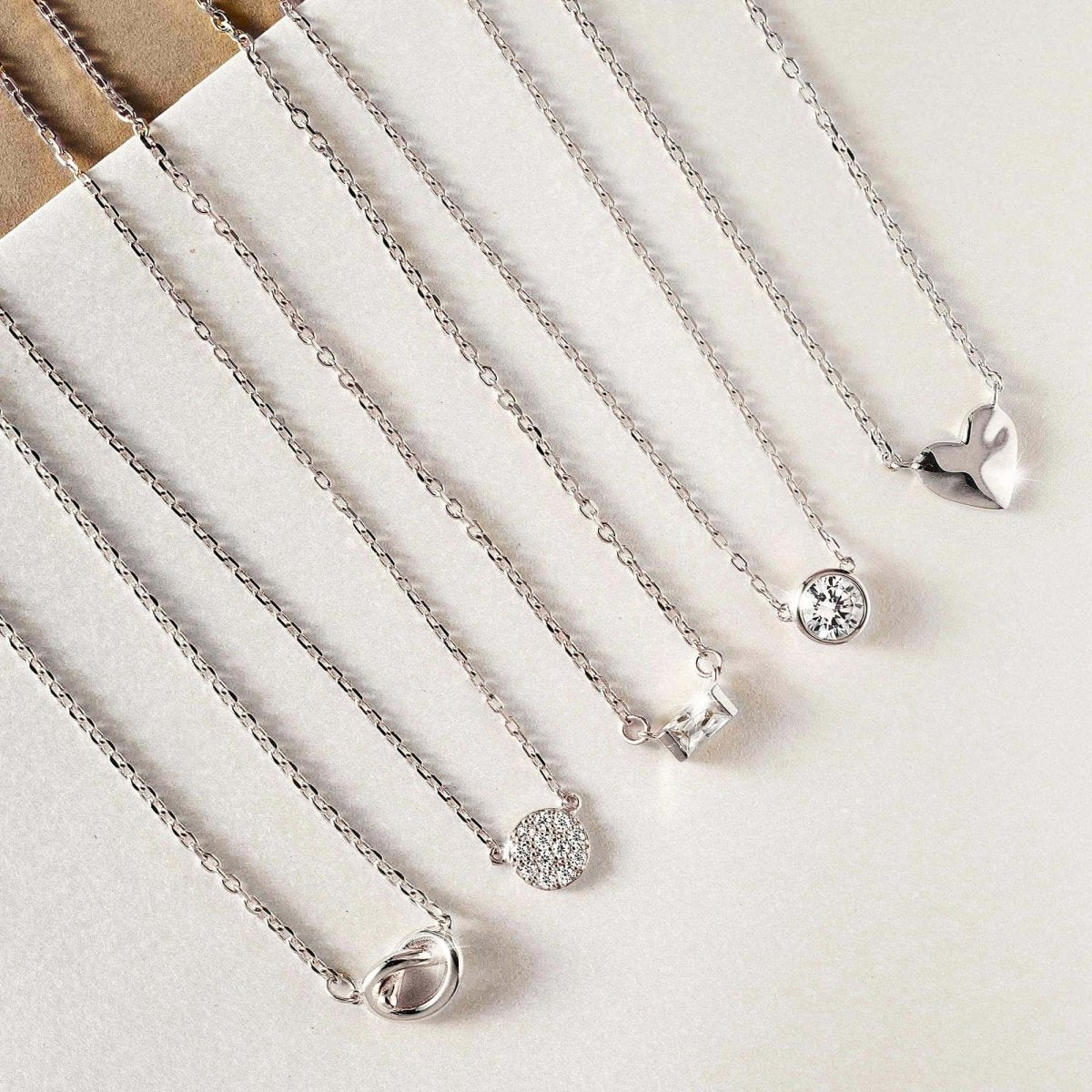 Sterling silver puffed heart pendant beside other pendant styles on chains, on a cream background