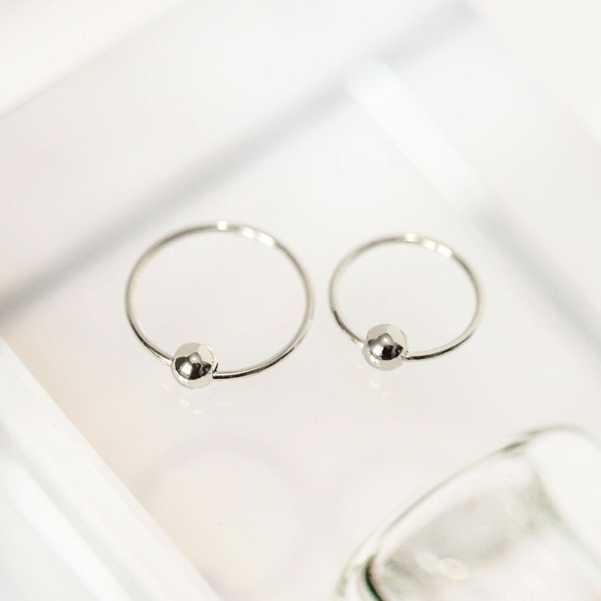 Pair of sterling silver captive bead hoops in two sizes, shown on a white tray