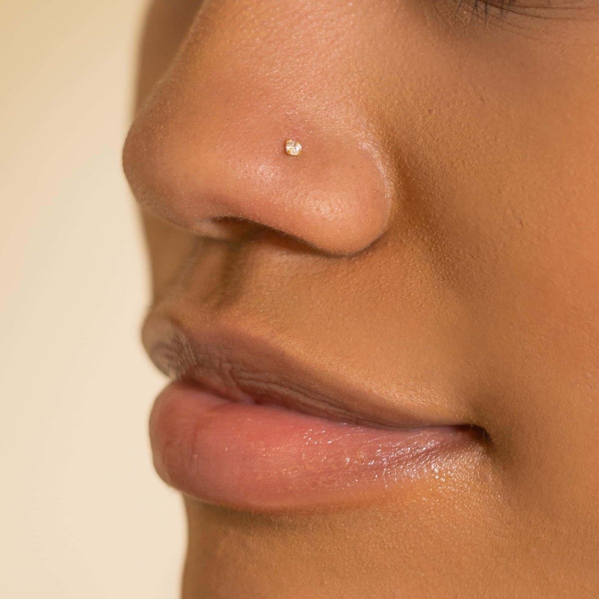 14K gold nose stud with a tiny white zirconia, shown on a model's nostril