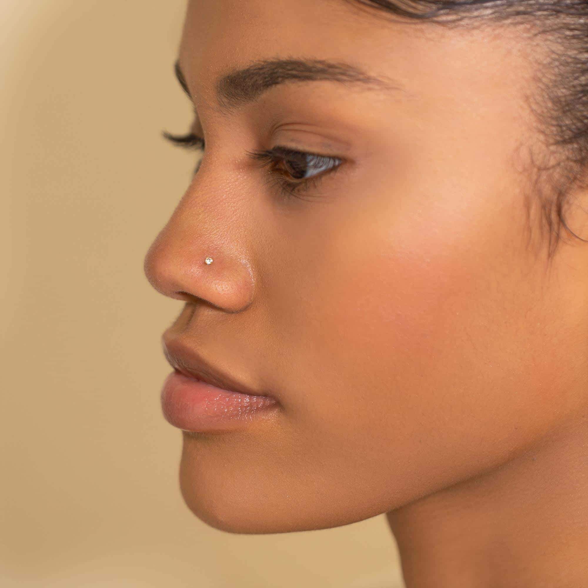 14K gold nose stud with a small white zirconia, shown on a model's nose in profile