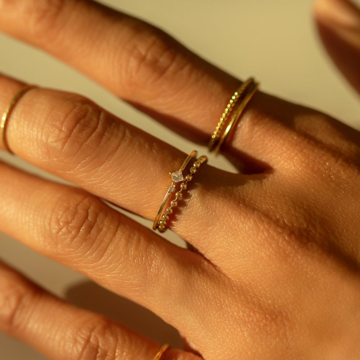 Gold-filled bead chain ring stacked with thin gold rings, close-up on a model's fingers