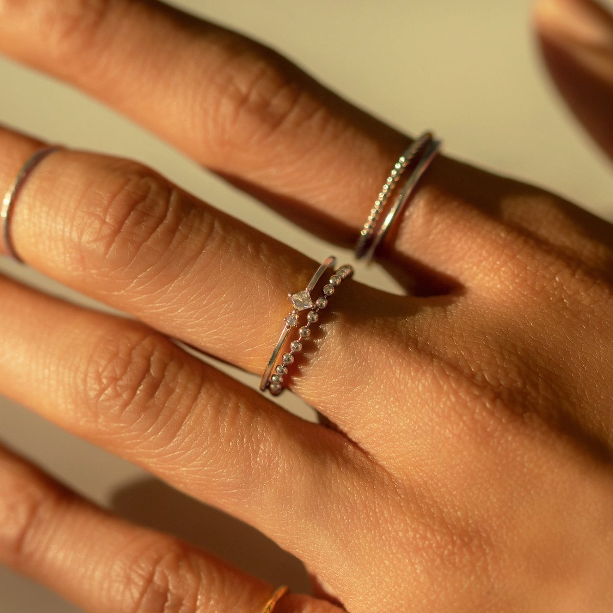 Sterling silver tiny duo ring stacked with thin beaded bands on a model's fingers