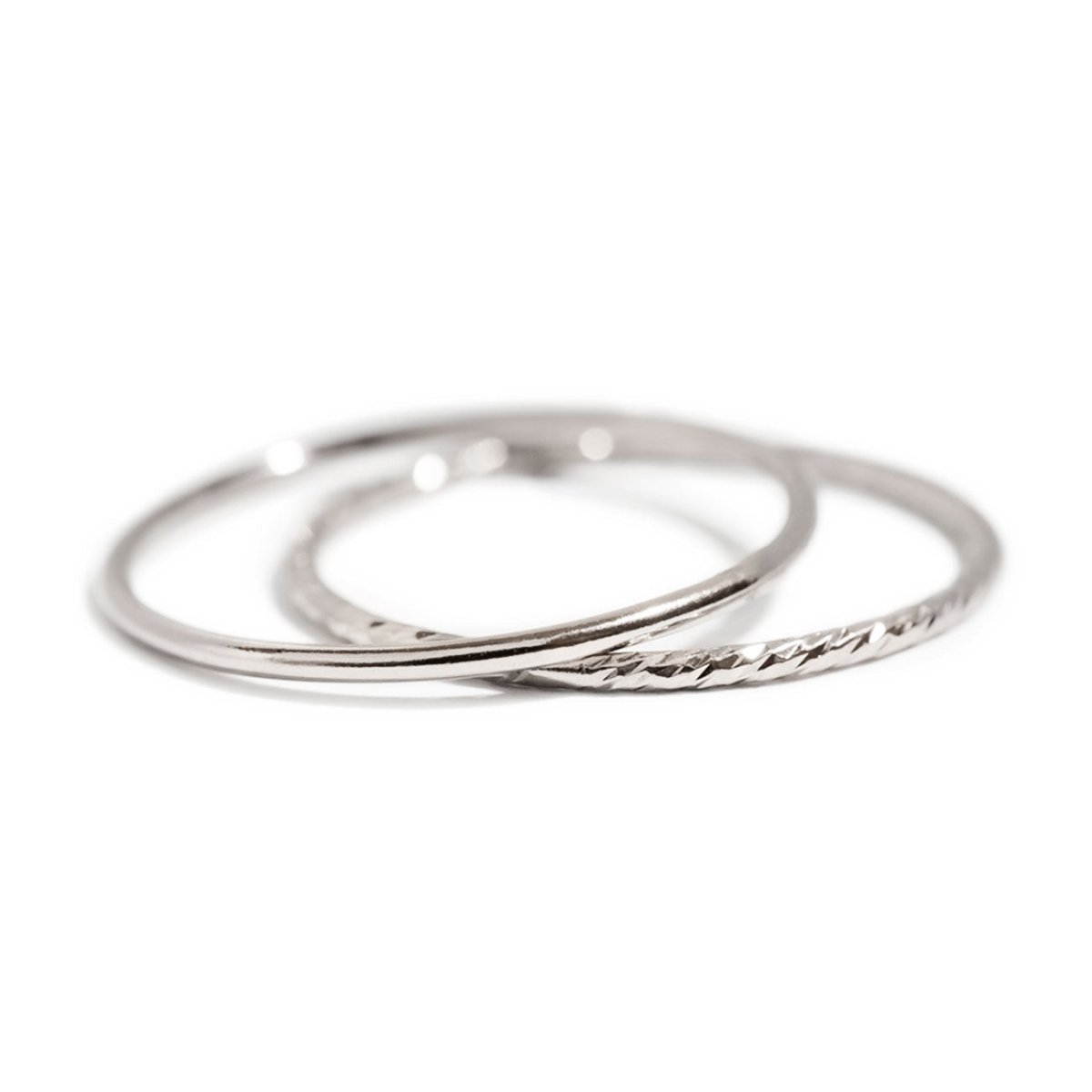 Sterling silver stacking rings, a smooth band and a faceted textured band, shown loose on a white background