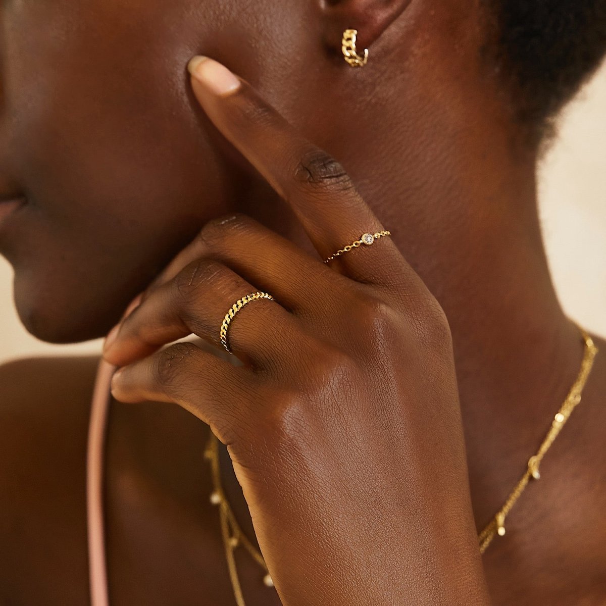 14K gold diamond chain ring with a bezel-set diamond, shown on a model's hand near a gold hoop and necklace