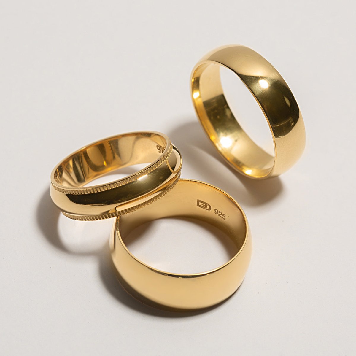 Three gold chunky domed band rings grouped together on a white background