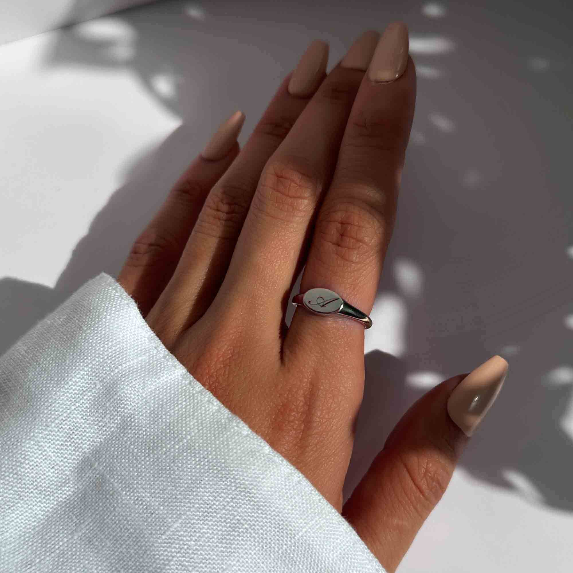 Sterling silver oval signet ring engraved with an initial, shown on a model's finger