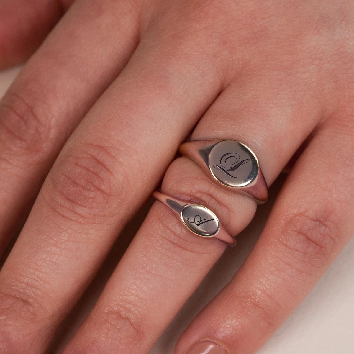Sterling silver oval signet rings engraved with initials, shown close-up on a model's fingers