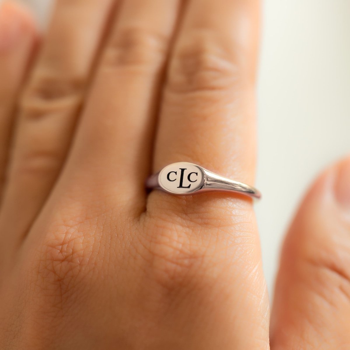 Sterling silver oval signet ring engraved with a monogram, shown on a model's finger