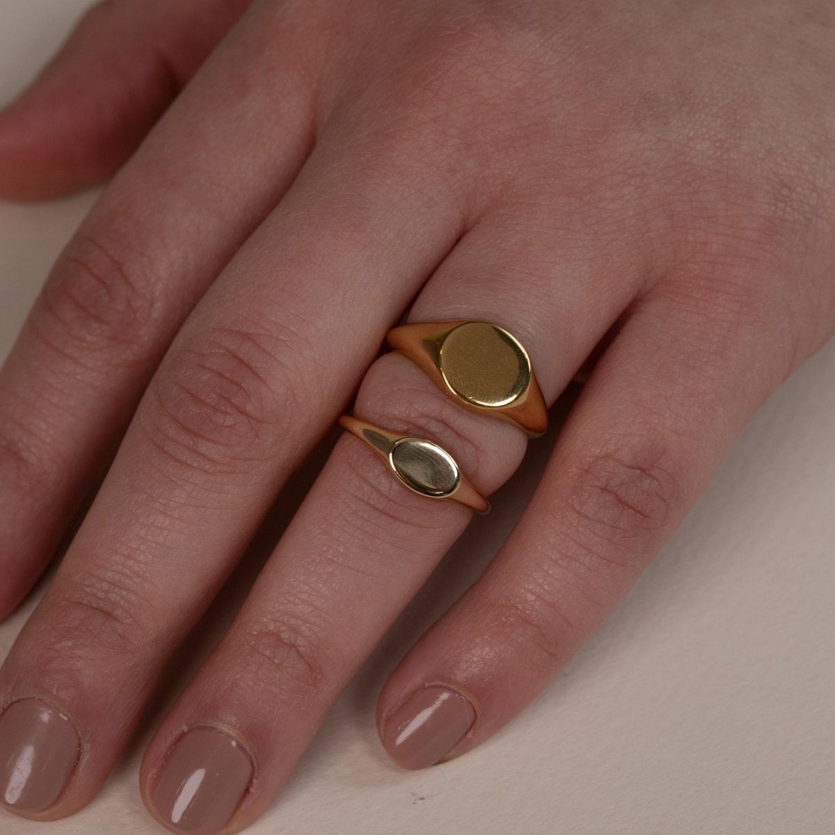 Gold vermeil oval signet rings with plain polished faces, shown close-up on a model's fingers