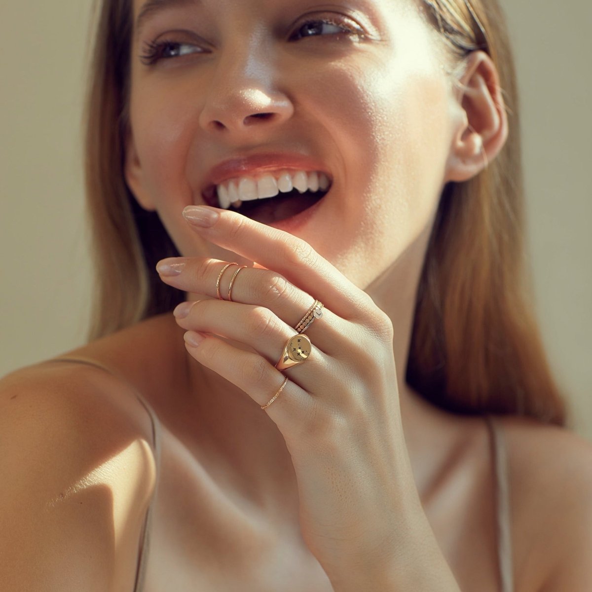 Gold-filled stacked disc and heart initial rings shown on a smiling model's hand