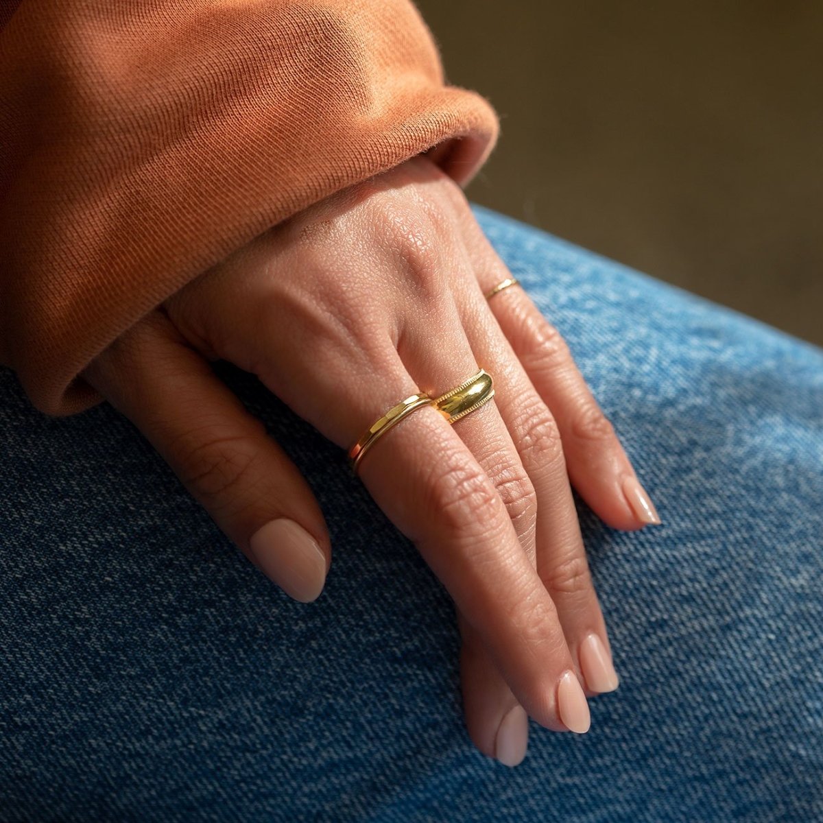 14K gold hammered thin stacking ring shown on a model's finger resting on denim