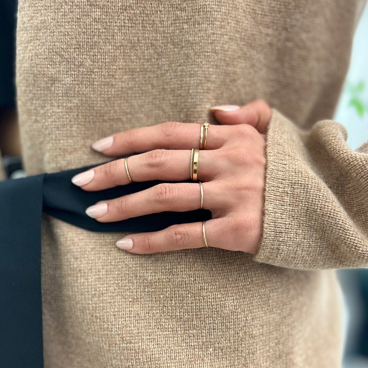 Gold-filled flat and rope band rings stacked on a hand resting on a tan sweater