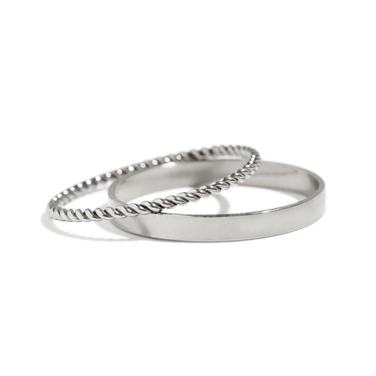 Sterling silver flat band and twisted rope band rings resting together, on a white background