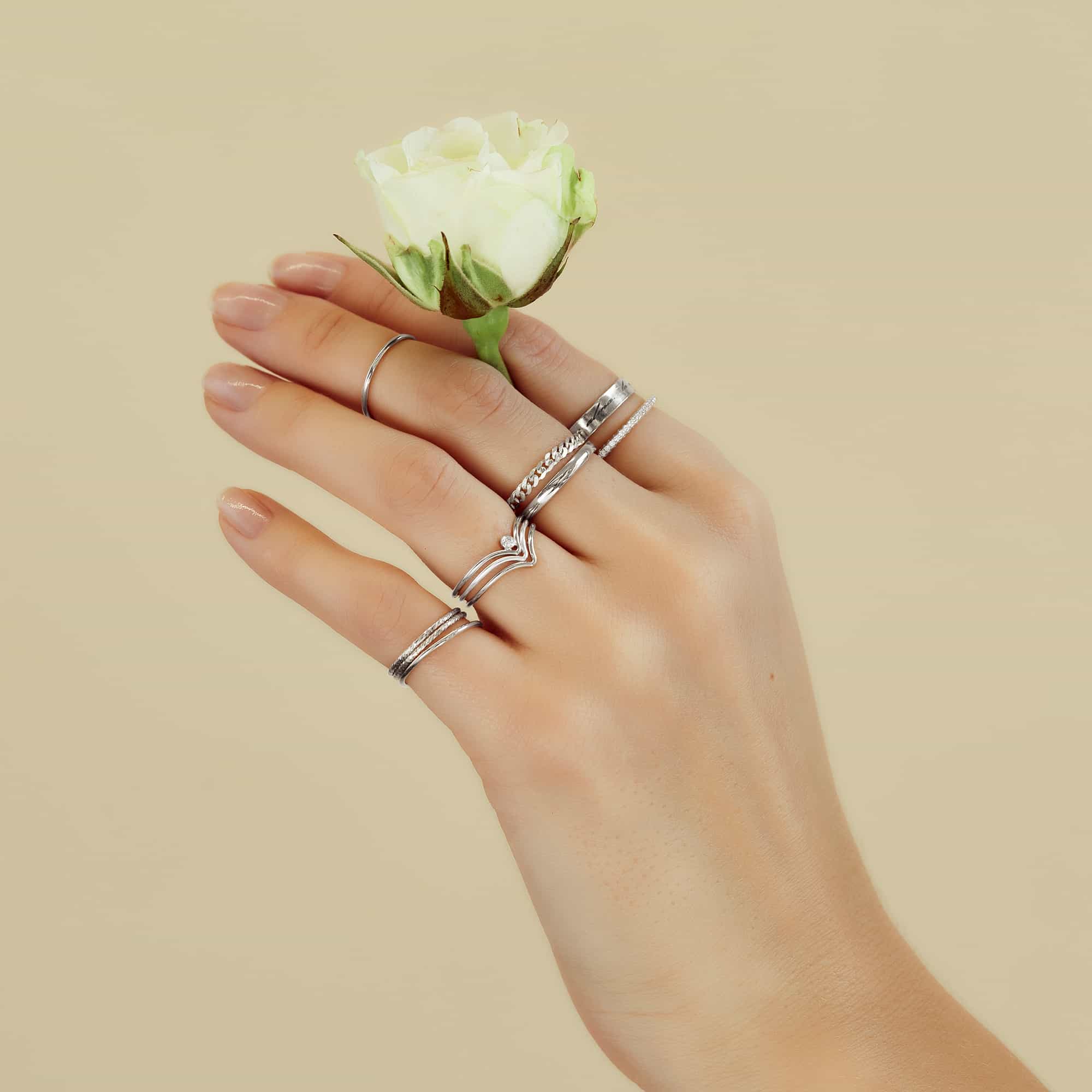 Sterling silver chevron ring stacked with other rings, on a model's hand holding a rose