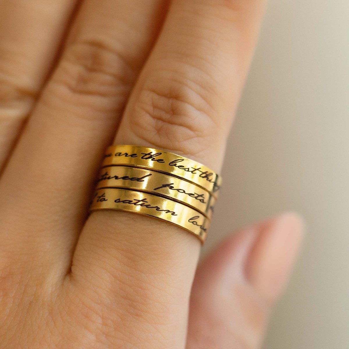 Gold-filled stacked band rings engraved with script messages, shown on a model's finger