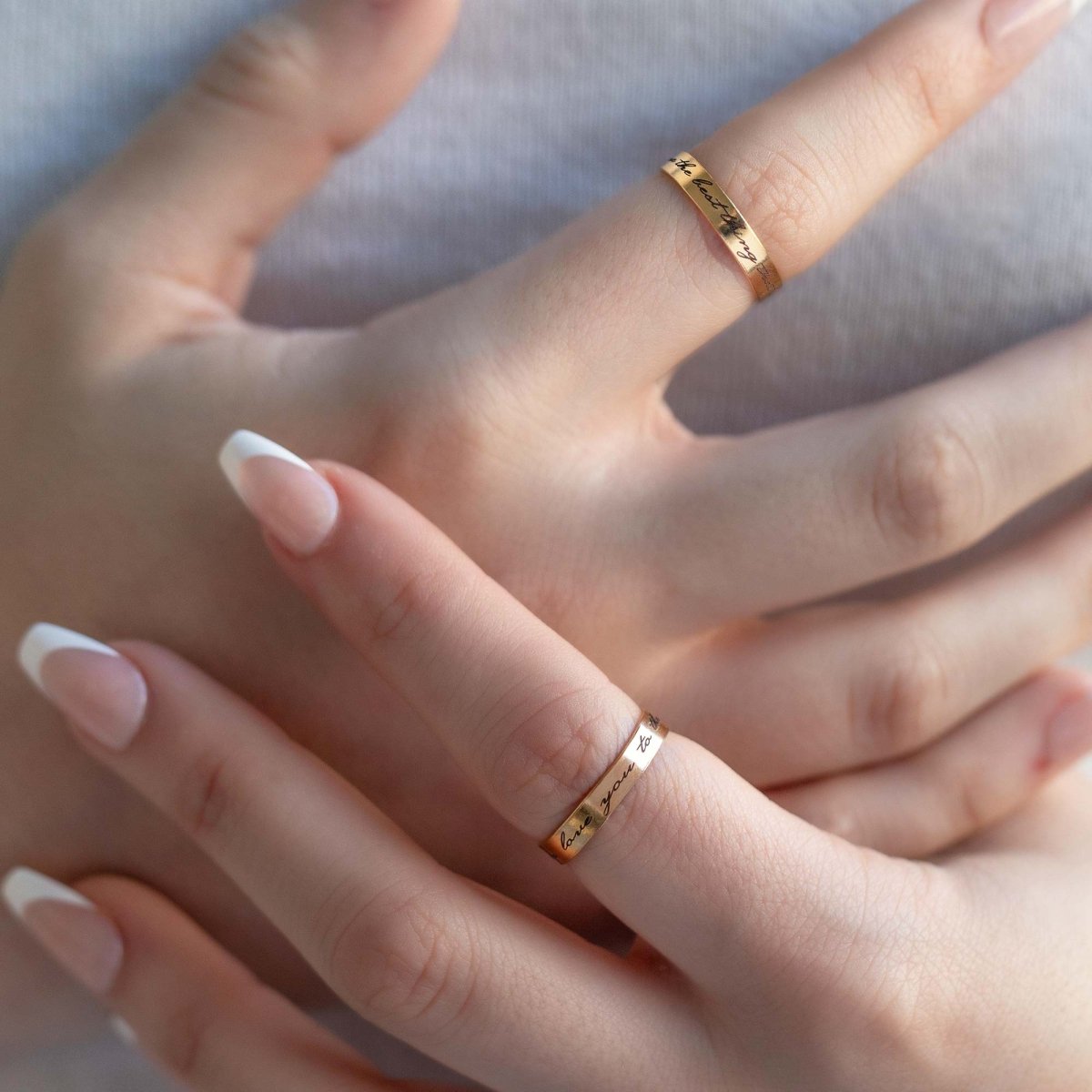 Gold-filled engraved band rings with script messages, shown on a model's two fingers