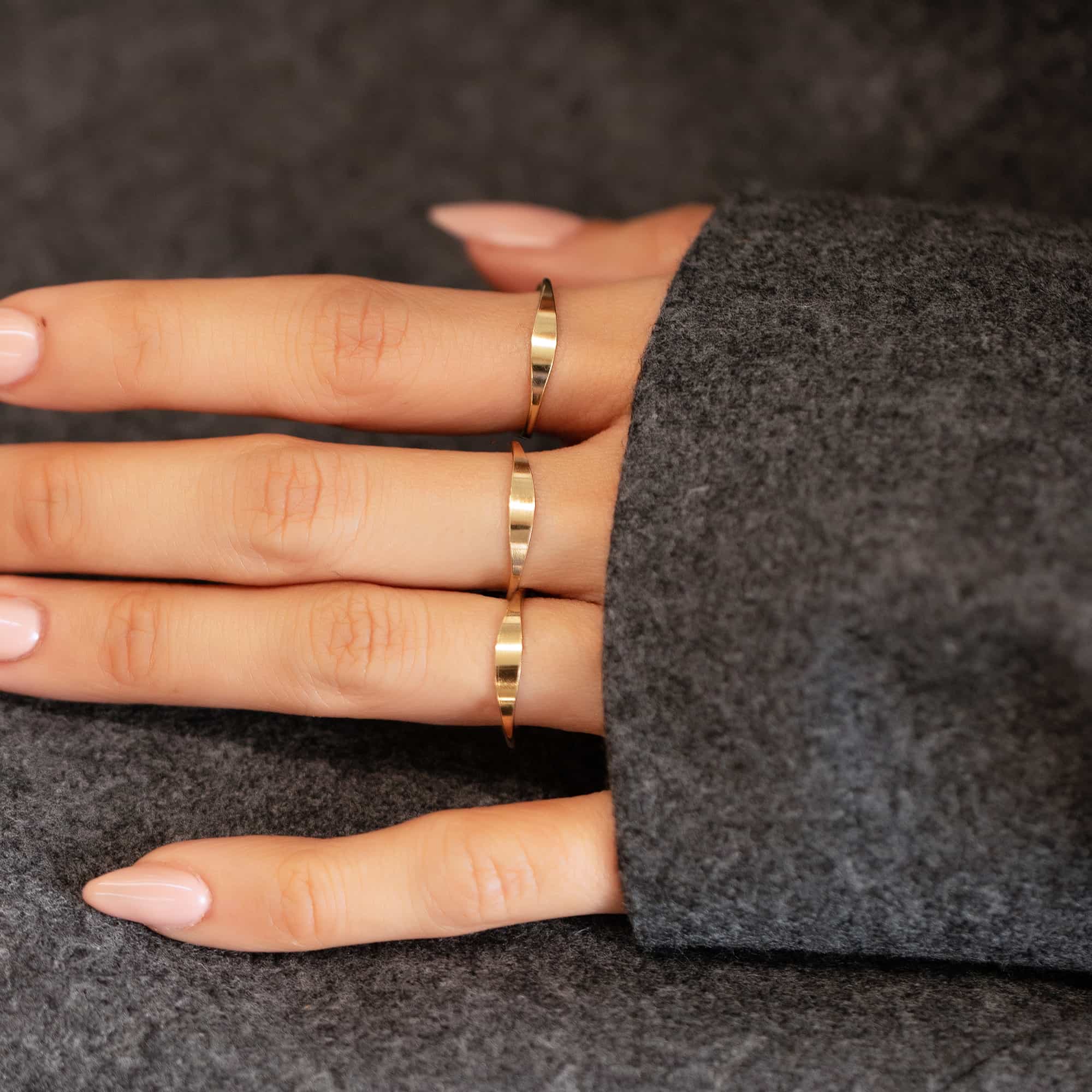 Gold-filled thin signet rings shown on three fingers against a grey wool sleeve
