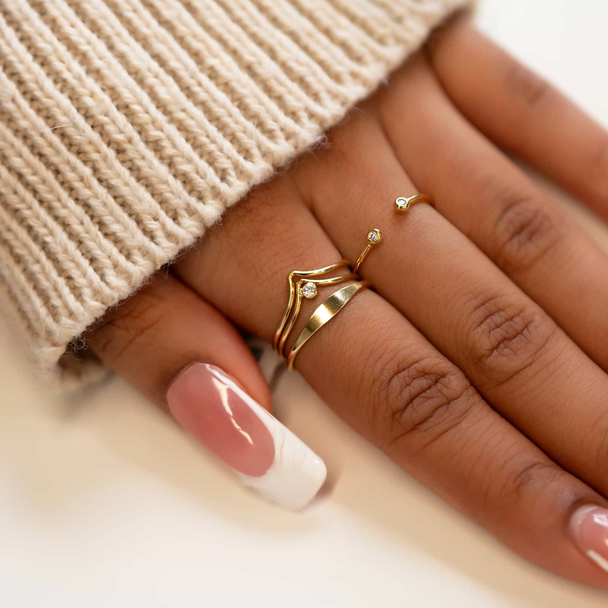 Gold-filled chevron ring with a clear stone, stacked on a model's hand resting on a cream background