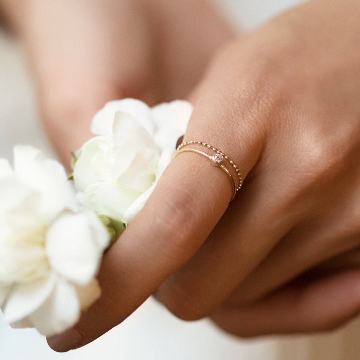 Gold-filled thin solitaire ring with white zirconia, shown on a model's hand near white flowers