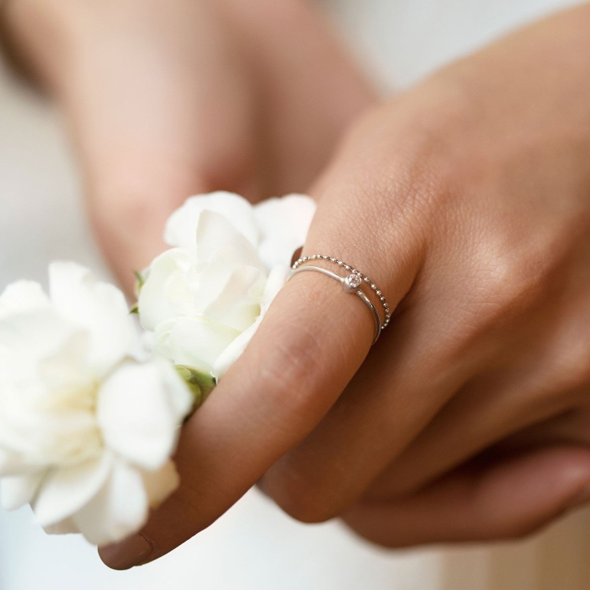 Sterling silver beaded chain ring shown on a model's finger with white flowers