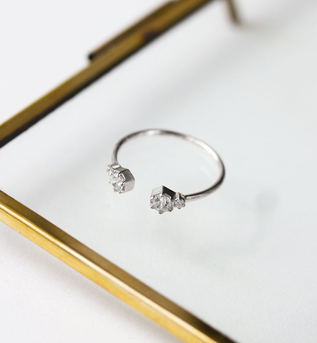 Sterling silver open cuff ring with clear zirconia stones, resting on a glass tray
