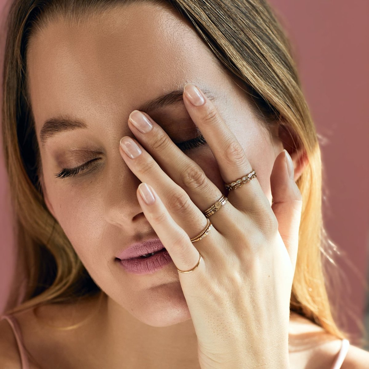 Gold-filled stacked initial rings shown on a model's fingers against her face