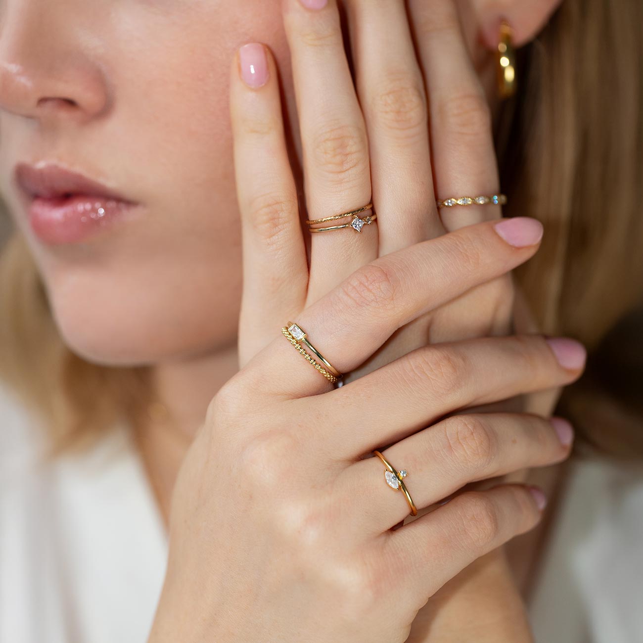 Gold thin stacking rings with clear stones, shown on a model's hand by her face