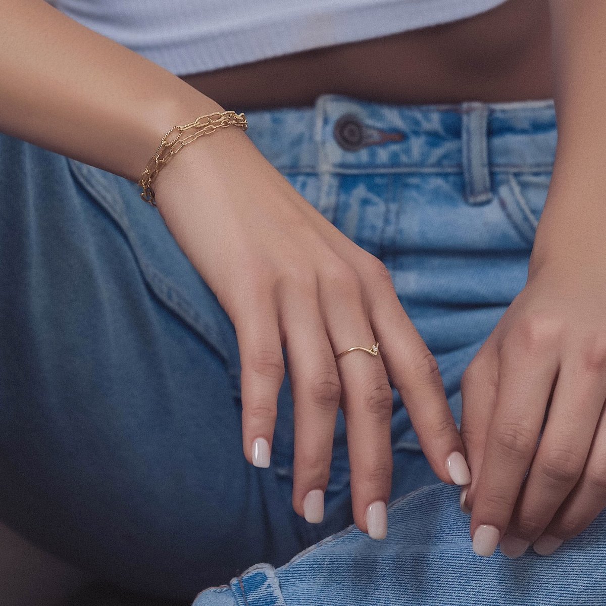 Gold vermeil chevron ring with a single clear stone, shown on a model's finger with jeans