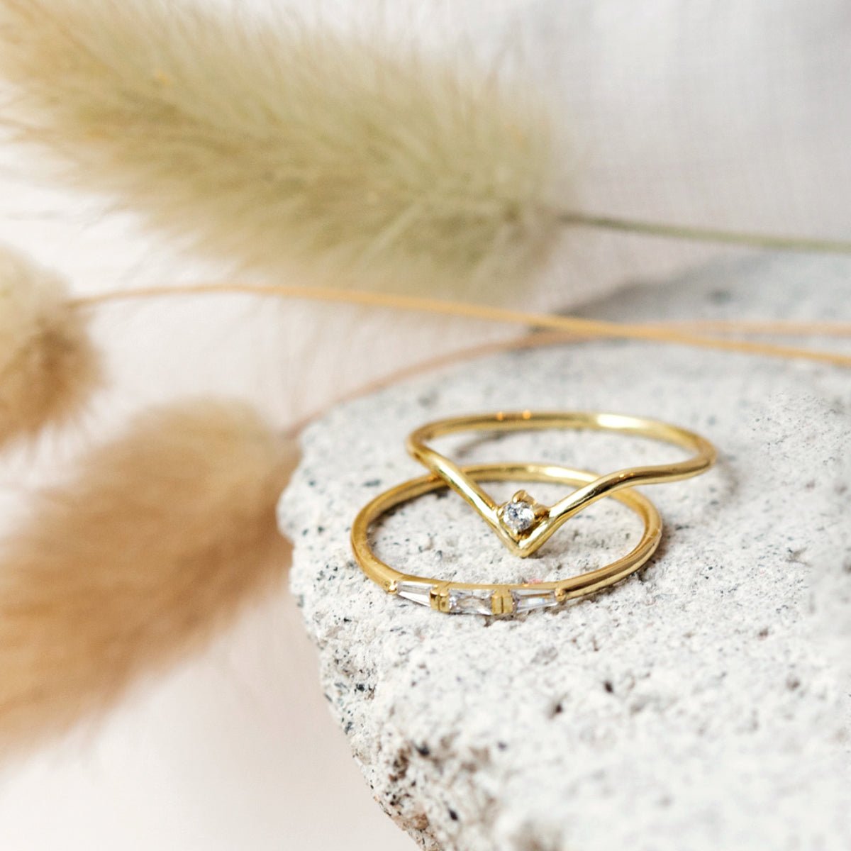 Gold vermeil chevron pavé ring set with clear stones, stacked on a stone slab with dried grass