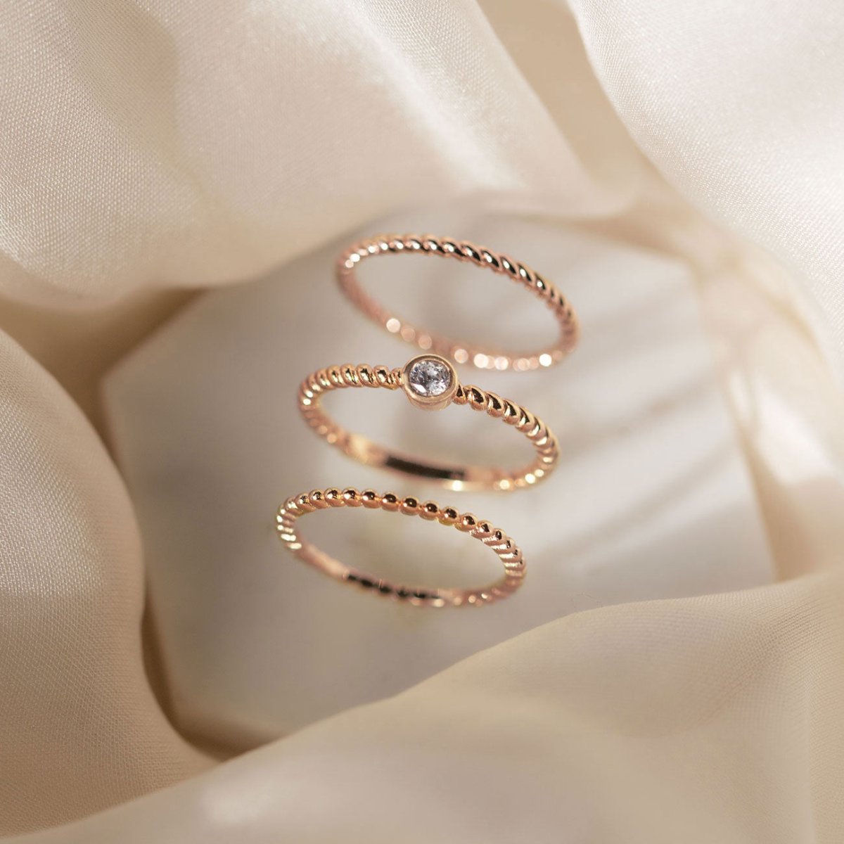 Rose gold vermeil solitaire rope ring with a clear stone, stacked with beaded bands on a cream background