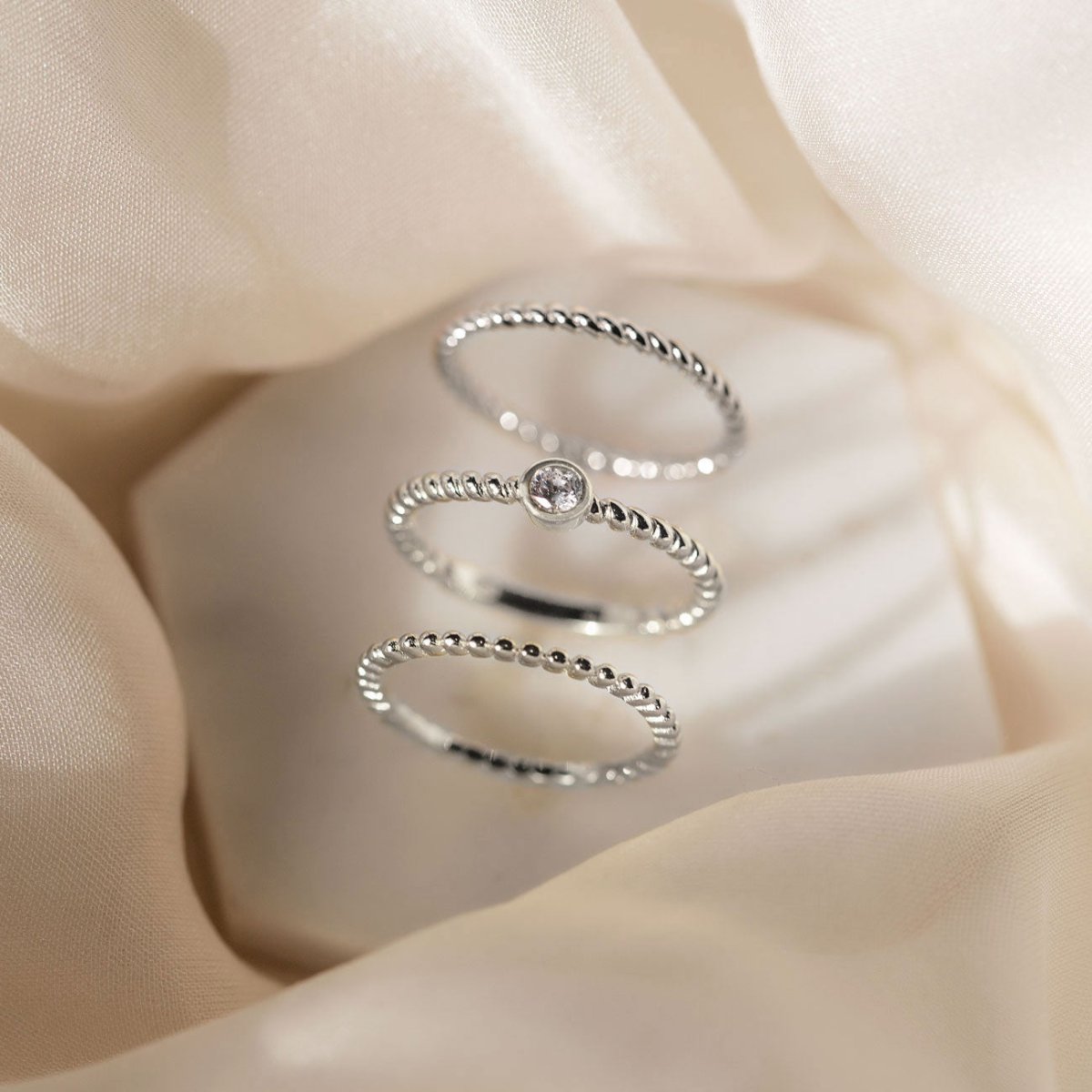 Sterling silver solitaire rope ring with a clear stone, stacked with beaded bands on a cream background