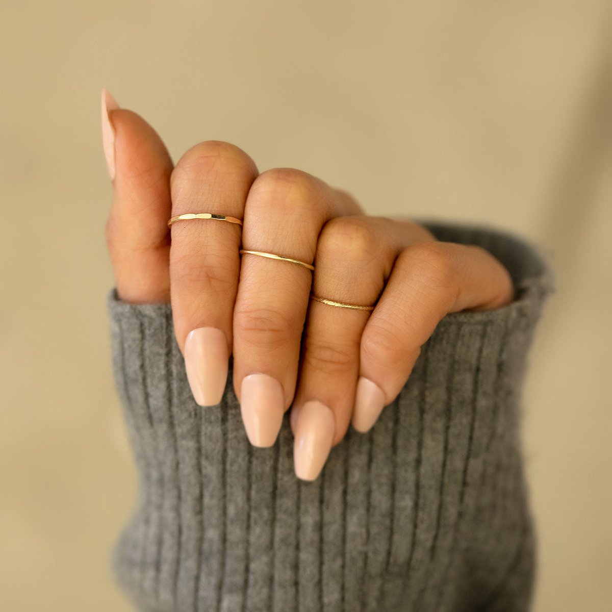 14K gold thin hammered stacking rings shown layered on a model's fingers