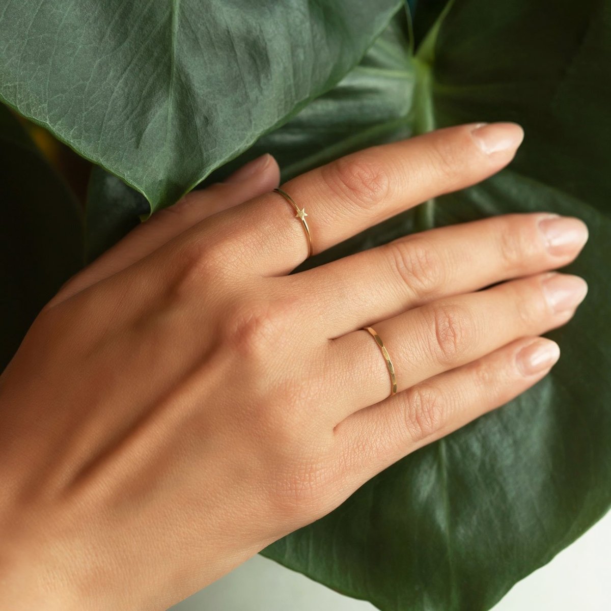 14K gold hammered thin stacking rings shown on a model's fingers against a green leaf