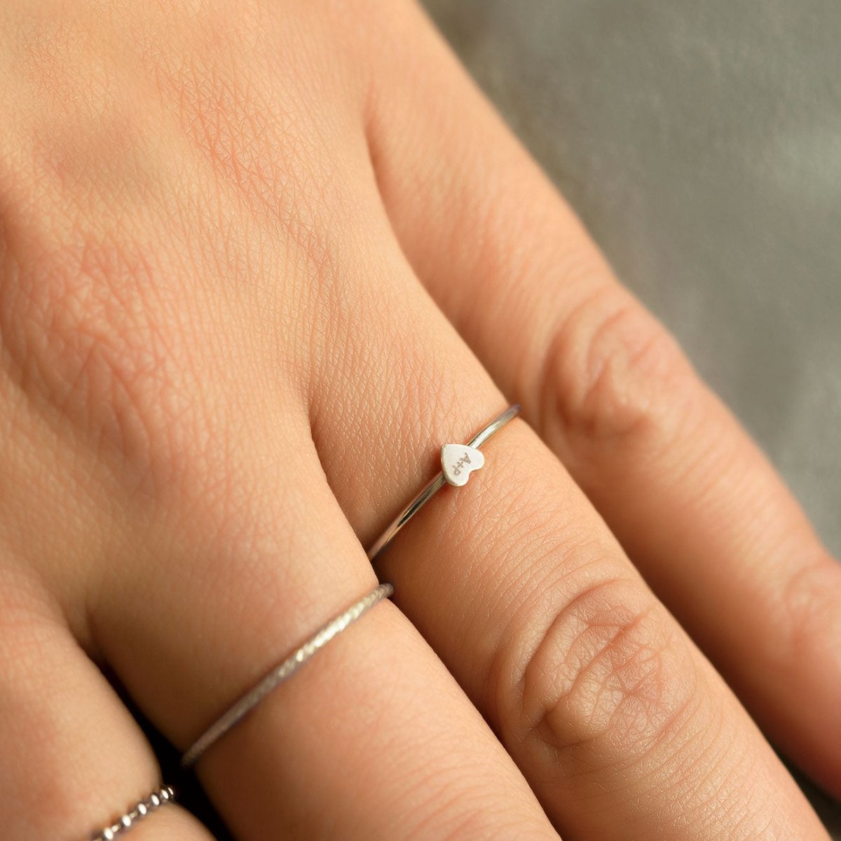 Sterling silver tiny heart ring engraved with initials, close-up on a model's finger
