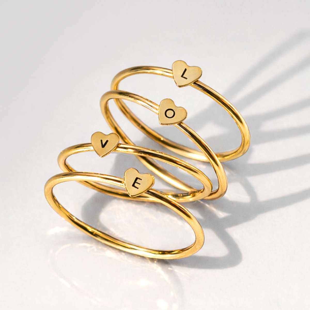 Set of gold-filled thin heart rings, each engraved with an initial, stacked on a light background