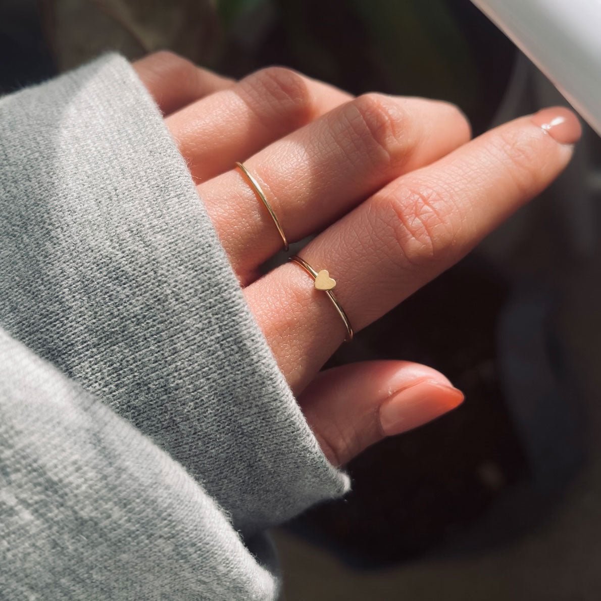 Gold-filled thin heart ring shown on a model's finger in sunlight