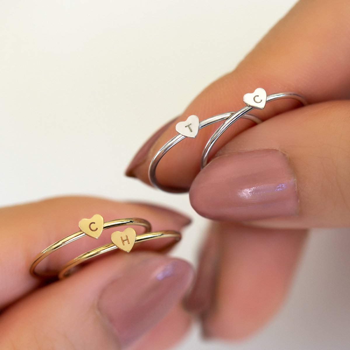 Sterling silver thin heart initial rings shown held between a model's fingertips