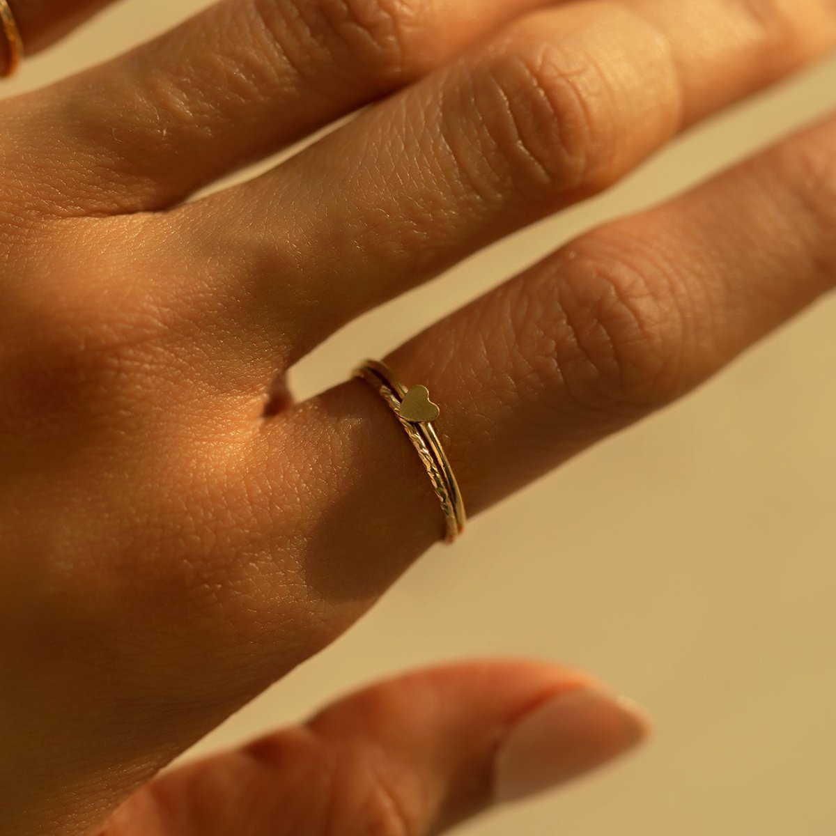 Gold-filled tiny heart stacker rings close-up on a model's finger in warm light