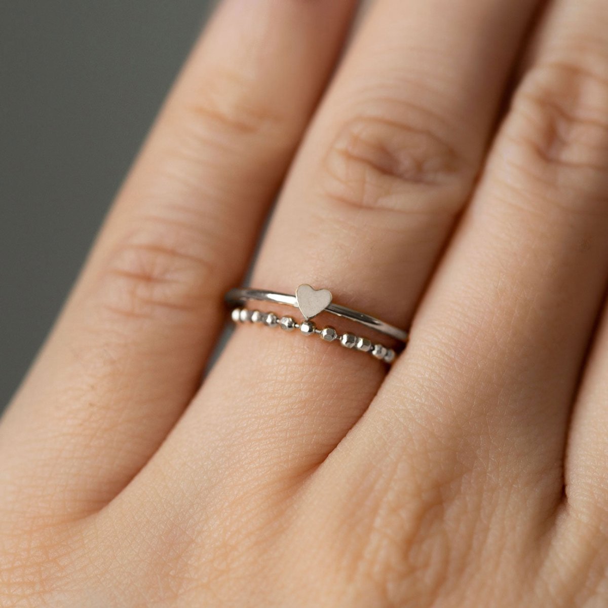 Sterling silver thin heart ring stacked with a beaded band, shown on a model's finger