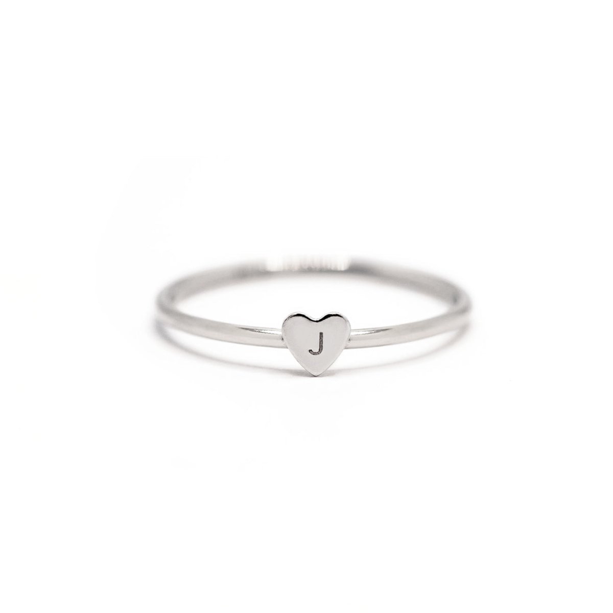 Sterling silver thin band ring with a tiny heart engraved with an initial, on a white background