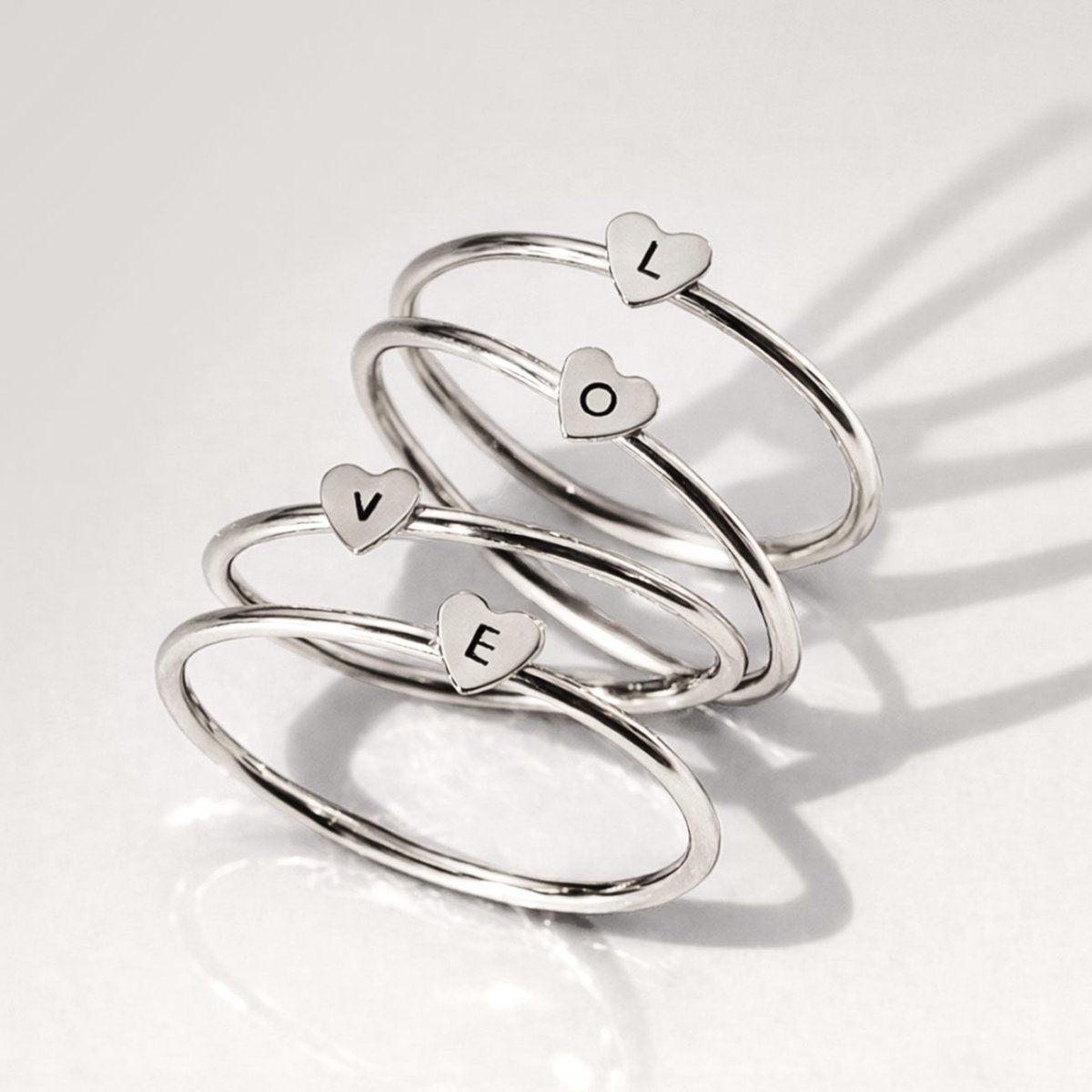 Set of sterling silver thin heart rings, each engraved with an initial, stacked on a light background