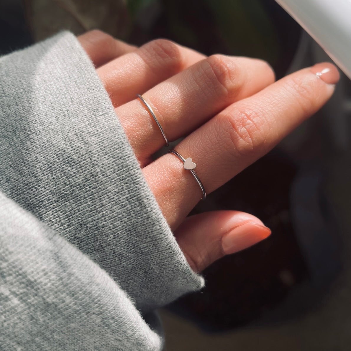 Sterling silver thin heart ring shown on a model's finger in sunlight