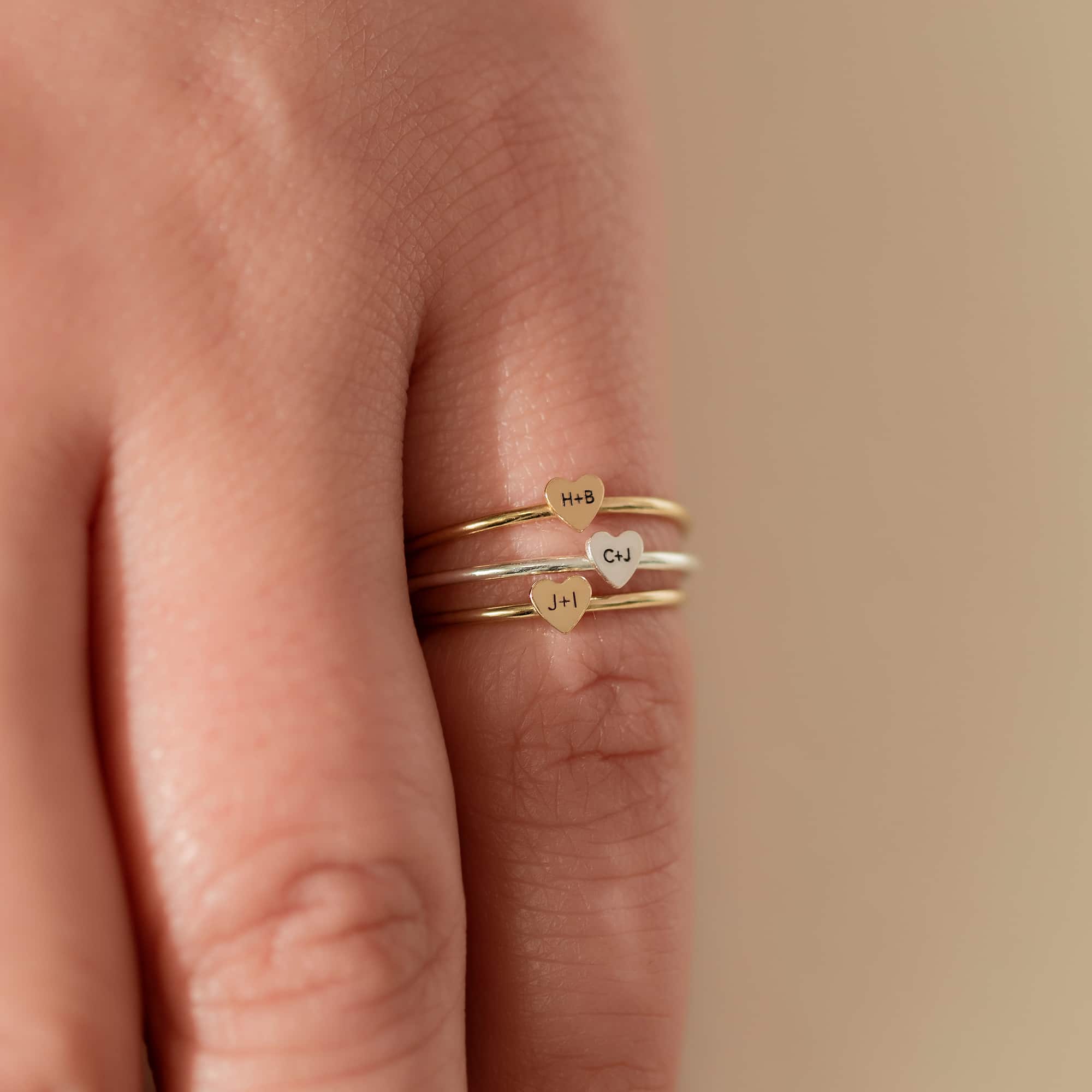 Sterling silver and gold-filled tiny heart initial rings engraved with letters, stacked on a finger