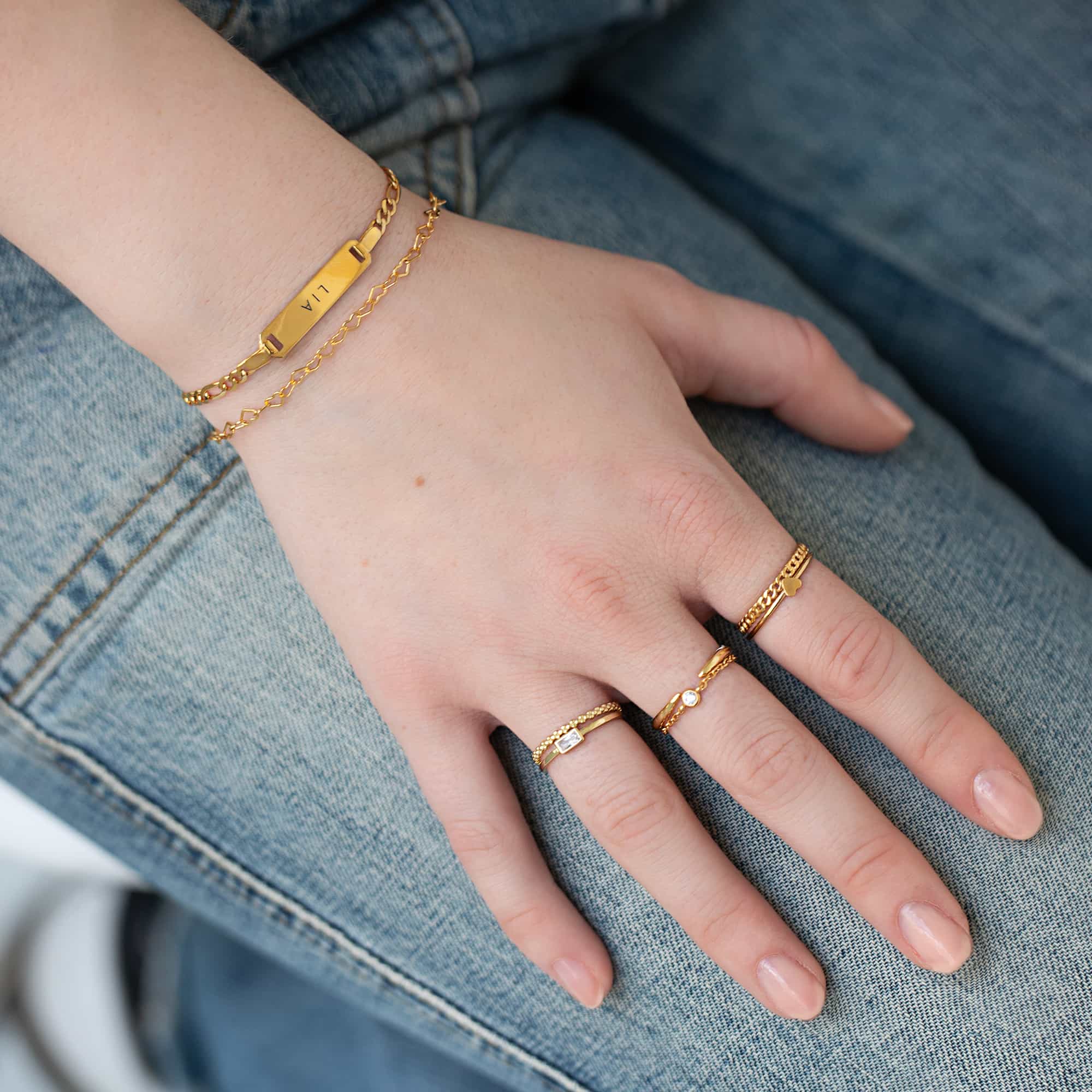 Gold bar bracelet engraved with a name and thin stacking rings shown on a model's hand
