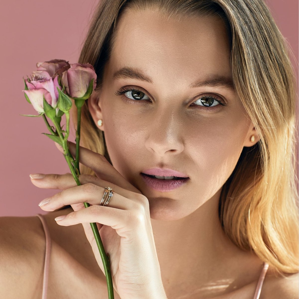 Gold-filled tiny heart initial ring with delicate stud earrings, shown on a model's hand by a rose